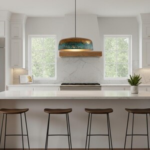 May include: A modern kitchen with white cabinetry, a stainless steel refrigerator, and a large island with four wooden stools. A pendant light with a blue and gold finish hangs above the island. Windows provide natural light.