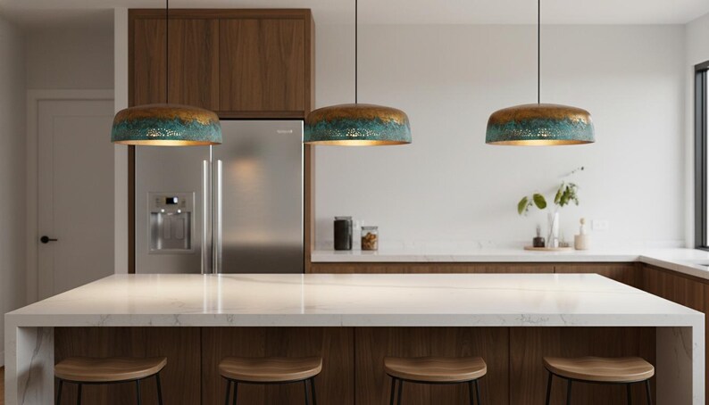 May include: A modern kitchen with three pendant lights. The lights have a bronze top, turquoise middle, and gold interior. The kitchen features a white countertop, wooden cabinets, and a stainless steel refrigerator. Wooden stools are at the island.