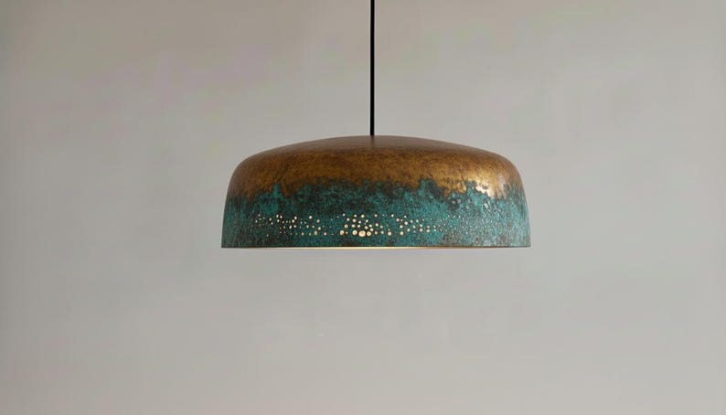 May include: A bronze and teal pendant light fixture. The top is a warm bronze color, transitioning to a teal hue at the bottom. Small, evenly spaced holes dot the teal section, allowing light to filter through.