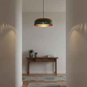 May include: A hallway with a pendant light fixture and a wooden console table. The light fixture has a copper-colored exterior and a gold interior. The console table has two potted plants and a stack of books.