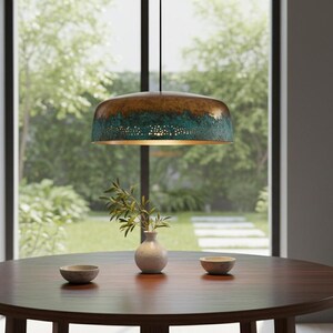 May include: A bronze and teal pendant light hangs above a dark wood table. The light fixture has a textured finish and a perforated lower section. A small white vase with greenery and two small bowls are on the table.
