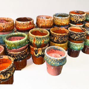 Peut inclure: Une collection de petites tasses en céramique présentant une variété d'émaux réactifs dans des tons orange, rose, bleu, vert et marron. Chaque tasse présente un motif de coulure distinct le long du bord, avec des surfaces intérieures lisses.