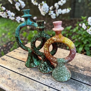 Peut inclure: Trois vases en céramique avec un design circulaire unique. Les vases sont dans les tons de turquoise, de vert et un dégradé de rouge, jaune et vert. Ils ont une texture tachetée et sont posés sur une surface en bois.