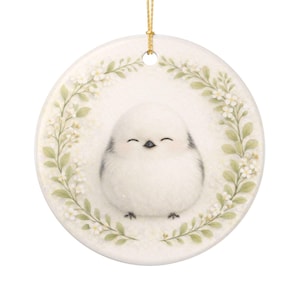 May include: A round, white ceramic ornament featuring a smiling, fluffy bird illustration. The bird is surrounded by a wreath of green leaves and white flowers. A gold string is attached for hanging. A charming, decorative item.
