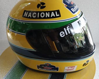 May include: A yellow racing helmet with green and black stripes, featuring the word "NACIONAL" and the "elf" logo. The helmet has a dark visor and the "Rothmans Racing" logo.