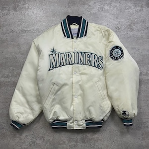 May include: Cream-colored Seattle Mariners satin jacket with the team name in teal across the chest. Features a team logo patch on the sleeve and navy, teal, and white striped trim on the collar, cuffs, and hem. A Starter logo is visible on the cuff.