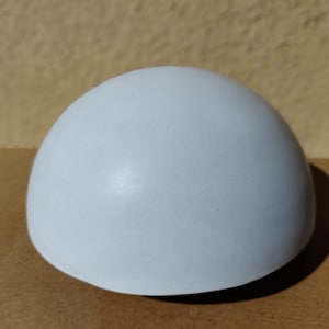 Può includere: Un oggetto emisferico bianco opaco e liscio con una forma a cupola arrotondata e pulita. La superficie è uniforme nel colore e nella consistenza, caratterizzata da una forma geometrica semplice che curva regolarmente dalla base alla cima.