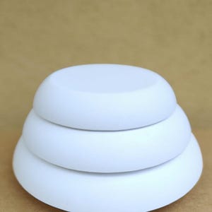 May include: A stack of three white, rounded, disc-shaped objects. The objects are arranged in a tiered formation, with the largest disc at the bottom and the smallest at the top. The objects are smooth and have a matte finish.