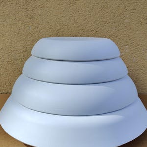 May include: Four pale blue, round, nested serving bowls of different sizes. The bowls are stacked, with the largest at the base and the smallest at the top. They have a smooth, matte finish. Ideal for serving.