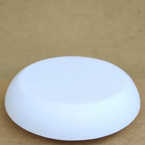 May include: A smooth, white, oval-shaped object. The object is a solid color and appears to be made of a matte material. The background is a light brown color.
