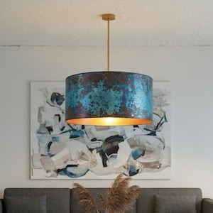 May include: A modern living room with a gray sofa, two light gray armchairs, and a white coffee table. A large abstract painting hangs above the sofa, and a unique blue and gold pendant light hangs from the ceiling.