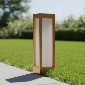 Può includere: Un'apparecchio di illuminazione per esterni di forma rettangolare color rame. Presenta un pannello bianco traslucido ed è posizionato su un prato verde accanto a un vialetto di cemento. Lo sfondo mostra alberi sfocati e un cielo blu. Altezza: circa 60 cm.