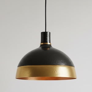 May include: A black and gold pendant light. The dome-shaped shade has a hammered texture and a gold band at the base. The light hangs from a black cord, creating a modern, elegant look. The diameter is approximately 30 cm.