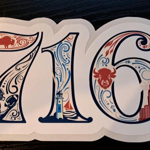 May include: A die-cut sticker featuring the number 716 in a decorative font. The design includes a red buffalo, a football player, a lighthouse, a sailboat, a red buffalo head, and a red building, all accented with blue and red scrollwork.
