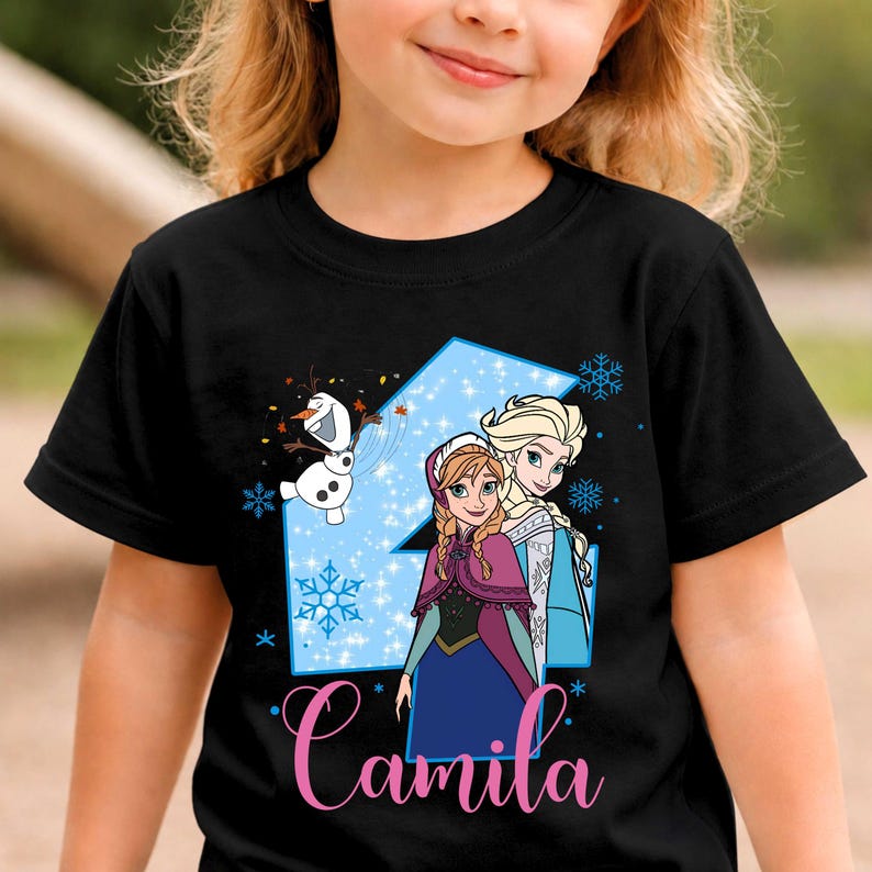 May include: A black short-sleeve t-shirt featuring a large light blue number four graphic with snowflakes, a cartoon snowman, and two animated characters. The name Camila is printed in pink cursive script at the bottom of the graphic design.