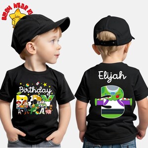 May include: Black short-sleeved t-shirt with a colorful graphic featuring characters from Toy Story and the text "Birthday Boy." The back of the shirt displays the name "Elijah" and a Buzz Lightyear design with the number "3."