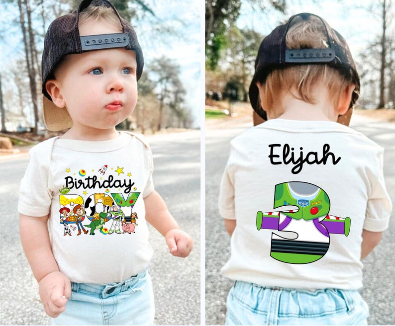 May include: A beige baby bodysuit with the words "Birthday BOY" and cartoon characters printed on the front. The back of the bodysuit has the name "Elijah" and a Buzz Lightyear graphic with the number "5". The child is wearing a black cap.
