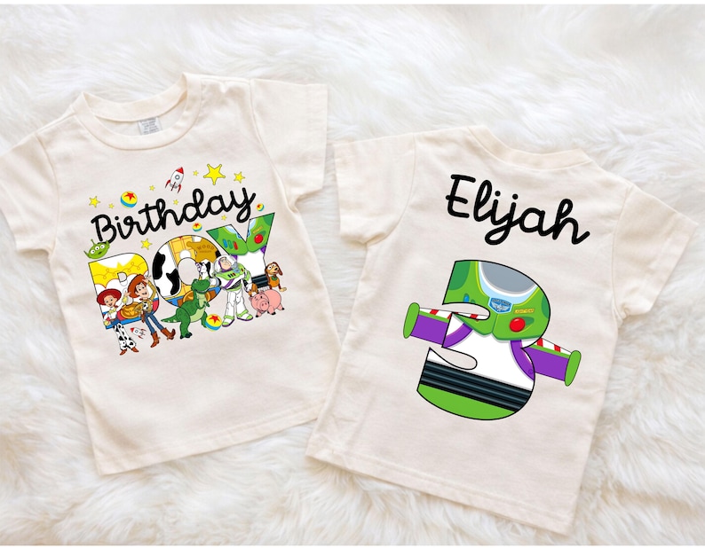 May include: Two cream-colored t-shirts. One features the text "Birthday BOY" with Toy Story characters. The other shirt has the name "Elijah" and a number "3" designed as Buzz Lightyear. Both shirts are short-sleeved.