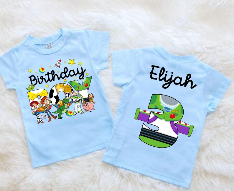 May include: Two light blue toddler t-shirts. One features the text "Birthday BOY" with Toy Story characters. The other shirt has the name "Elijah" and a Buzz Lightyear-themed number "3" graphic.
