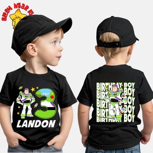 May include: Black t-shirt featuring a Buzz Lightyear graphic with the number 3 and the name "LANDON" in white. The back of the shirt has a Buzz Lightyear graphic and the words "BIRTHDAY BOY". The child is wearing a black baseball cap.