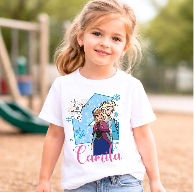 May include: A white short-sleeved t-shirt featuring a graphic print of the characters Anna, Elsa, and Olaf from Frozen. The design includes a large blue number four, light blue snowflakes, and the name Camila written in pink cursive script.