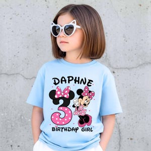 May include: A light blue t-shirt with the name "Daphne" and the number "3" in a pink polka dot design. A cartoon Minnie Mouse graphic is also on the shirt. The text "BIRTHDAY GIRL" is below the number.
