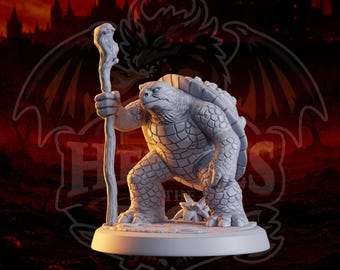 May include: A light grey miniature figurine of an anthropomorphic turtle standing on a circular base. The turtle has a textured shell, scaly skin, and is holding a tall, gnarled wooden staff in its right hand. The figure is sculpted with detail.