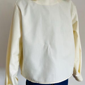 Può includere: Camicia a maniche lunghe color crema con colletto a stampa floreale a contrasto. Il colletto presenta uno sfondo giallo chiaro con motivi a foglie blu e verdi. La camicia ha polsini con bottoni.