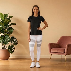 Puede incluir: Una persona con una camiseta negra y leggings blancos con rayas grises. La persona lleva zapatillas blancas. El fondo incluye una planta en maceta y un sillón rosa.