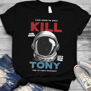 Könnte beinhalten: Schwarzes T-Shirt mit einer Grafik eines Astronautenhelms und dem Text "KILL TONY" in Rot und Blau. Zusätzlicher Text enthält "AIRING AROUND THE WORLD" und "EVERY MONDAY!" Das Shirt sagt auch "LIVE IN AUSTIN TEXAS!" und "FROM THE COMEDY MOTHERSHIP!"