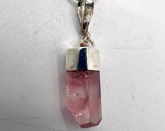 May include: A silver pendant necklace featuring a pink crystal pendant. The crystal is a light pink color with a faceted, geometric shape. The pendant is attached to a silver chain.