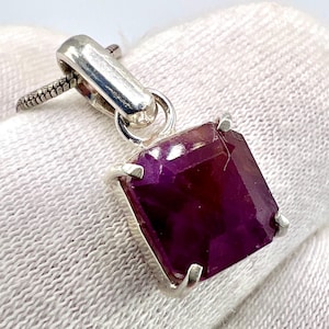 Pode incluir: Pingente de prata com uma grande pedra preciosa roxa escura com corte quadrado. A pedra preciosa é mantida no lugar por quatro garras de prata. O pingente pende de uma argola de prata e uma corrente de prata texturizada.