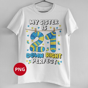 Op de afbeelding: Wit T-shirt met de tekst "MY SISTER IS 21 DOWN RIGHT PERFECT". Het cijfer 21 is ontworpen met blauwe en gele sokken. Het shirt heeft een ronde hals en korte mouwen.