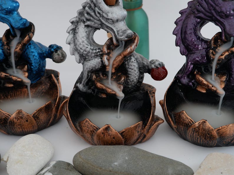 May include: Three dragon incense burners in blue, white, and purple. Each dragon sits atop a lotus flower base with a bronze finish. Incense smoke flows from the dragon's mouth, creating a mystical effect. Decorative home decor.