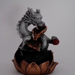May include: A decorative dragon figurine in silver, bronze, and red. The dragon is perched atop a lotus flower base. The figurine is a detailed sculpture, likely for home decor or spiritual practices.