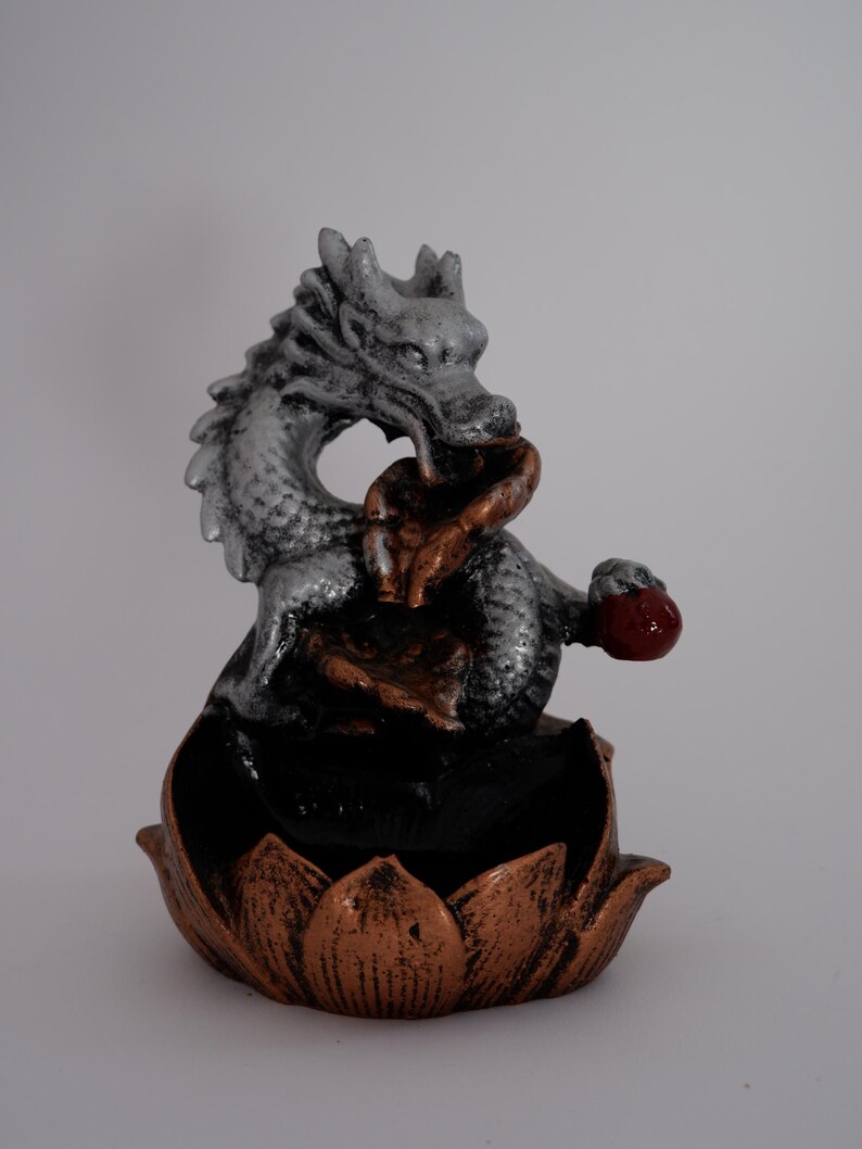 May include: A decorative dragon figurine in silver, bronze, and red. The dragon is perched atop a lotus flower base. The figurine is a detailed sculpture, likely for home decor or spiritual practices.