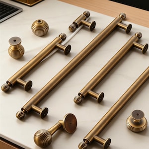 May include: Bronze-coloured cabinet hardware set, including long bar pulls, knobs, and a decorative sphere. The hardware features a vintage aesthetic with detailed, grooved accents. Ideal for kitchen or bathroom renovations.