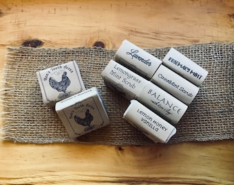 May include: Assortment of small, brown paper boxes with various labels. The labels include "Lavender", "Lemongrass Mint Scrub", "Rosemary Mint", "CinnaMint Scrub", "BALANCE with Rose Clay", "Lemon Honey Vanilla", and "Hen's Tooth Acres".