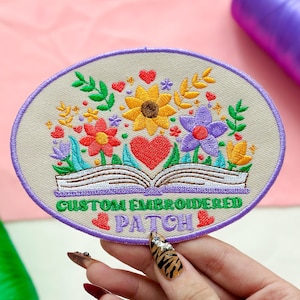May include: Oval embroidered patch featuring a floral design with a book at the base. The patch includes sunflowers, red and purple flowers, and the text "CUSTOM EMBROIDERED PATCH" in green and purple.