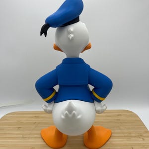Op de afbeelding: Een 3D-geprint beeldje van Donald Duck, van achteren gezien. De figuur is voornamelijk wit met oranje voeten en snavel. Hij draagt een blauw matrozenhemd en hoed met een zwarte strik. Gele biezen accentueren de mouwen.