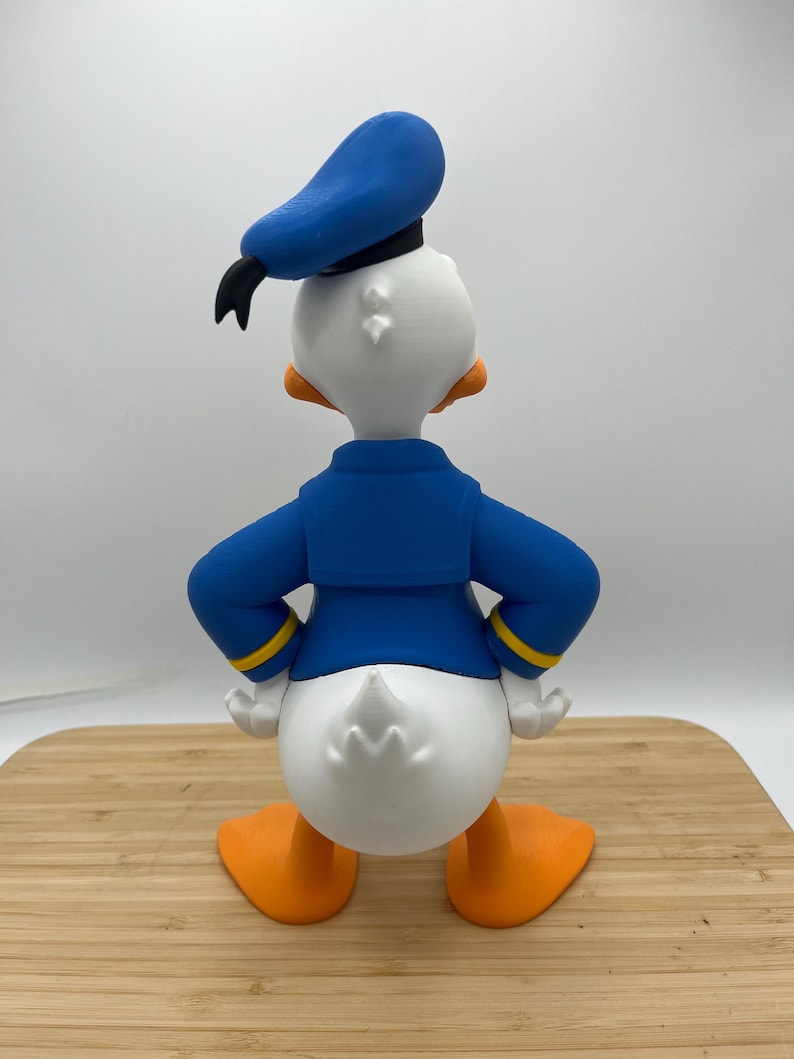 Op de afbeelding: Een 3D-geprint beeldje van Donald Duck, van achteren gezien. De figuur is voornamelijk wit met oranje voeten en snavel. Hij draagt een blauw matrozenhemd en hoed met een zwarte strik. Gele biezen accentueren de mouwen.