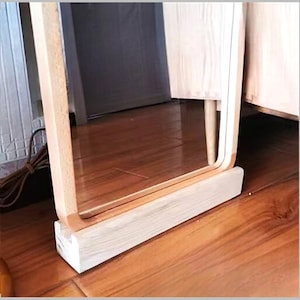 Puede incluir: Un espejo rectangular de madera clara con esquinas redondeadas. El espejo está colocado sobre una base rectangular de madera clara. El espejo refleja el entorno.