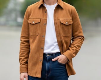 Peut inclure: Une chemise en daim marron avec deux poches de poitrine et des boutons. La chemise est portée sur un t-shirt blanc et associée à un jean bleu. Le modèle a une main dans sa poche.