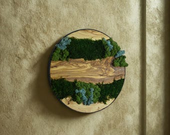 以下が含まれることがあります： 木材をベースにした丸い壁掛けアート。天然の木目が特徴で、緑と青の苔で装飾され、自然な質感を演出。黒い金属リングで縁取られ、インテリアに最適です。