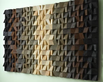 Op de afbeelding: Een groot, rechthoekig houten wandkunstwerk. Het kunstwerk bestaat uit talrijke kleine, schuine houten blokken die zo zijn gerangschikt dat er een gradiënteffect ontstaat. De kleuren lopen over van lichtbeige naar donkerbruin en zwart, waardoor een textuur en driedimensionaal uiterlijk ontstaat.