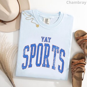 a light blue t-shirt with the text "YAY SPORTS" printed on it, along with a beige hat and sandals.