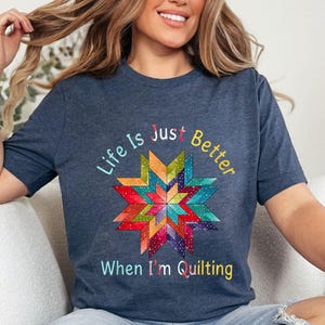 May include: Navy blue t-shirt with a colorful starburst quilt design. The shirt features the text "Life Is Just Better When I'm Quilting" in a rainbow of colors. A comfortable tee for quilters.