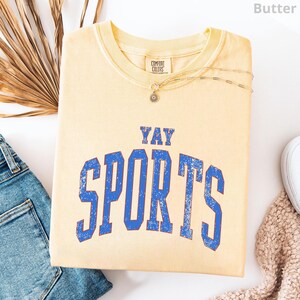 a yellow t-shirt with the text "YAY SPORTS" printed on it, along with a denim jacket and some other clothing items.