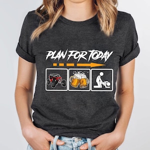 Könnte beinhalten: Dunkelgraues T-Shirt mit dem Text "PLAN FOR TODAY" über drei illustrierten Symbolen: einem roten Geländewagen, zwei Bierkrügen und einer Strichmännchen-Figur. Das T-Shirt hat einen Rundhalsausschnitt und kurze Ärmel.