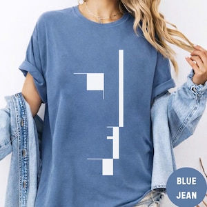 May include: A blue short-sleeved t-shirt featuring a white graphic design composed of vertical and horizontal lines and a square. The shirt is worn with a blue denim jacket. The design is centered on the chest of the garment.
